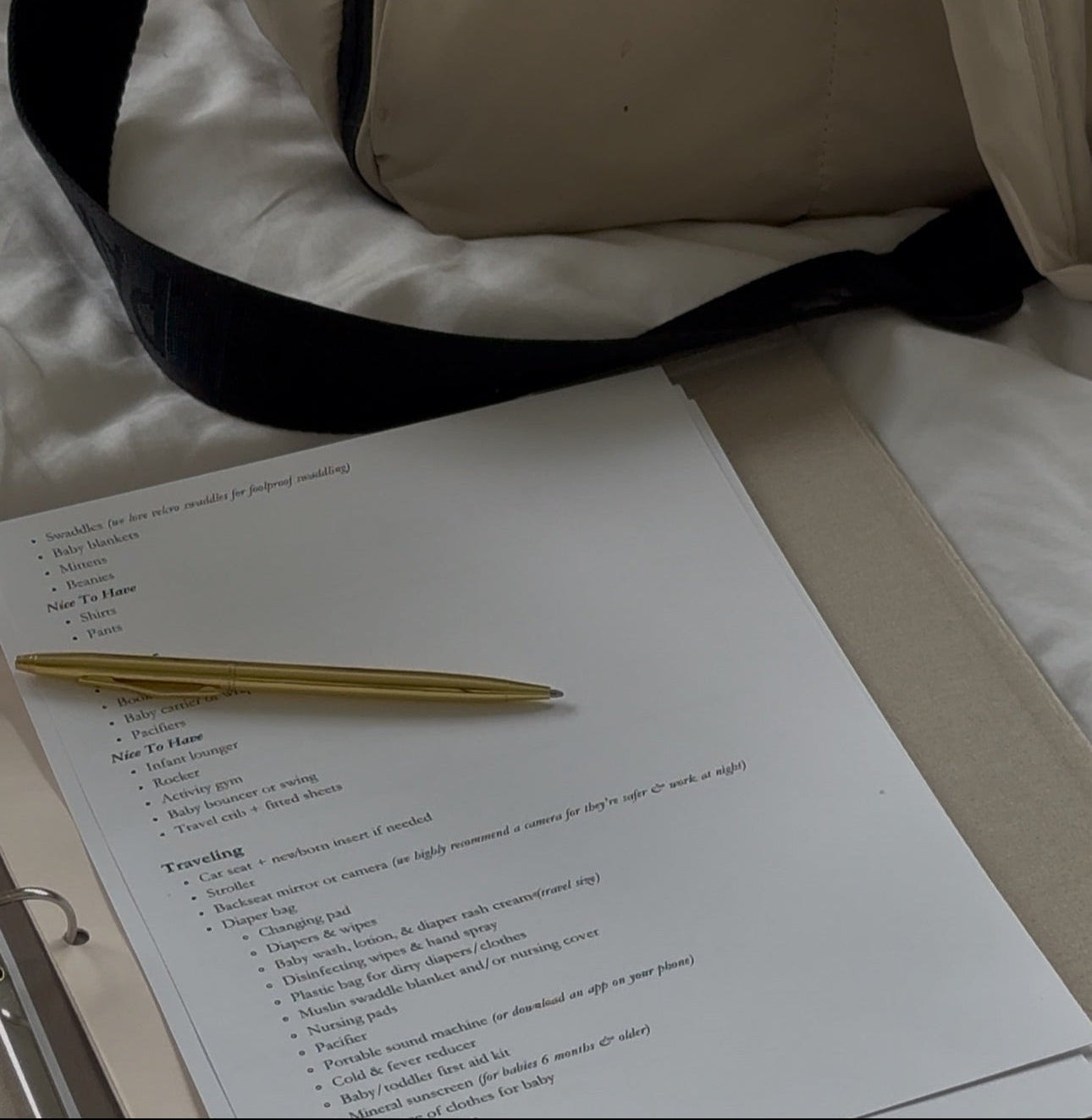 nursery checklist with a gold pen on a white surface, with a beige bag in the background.